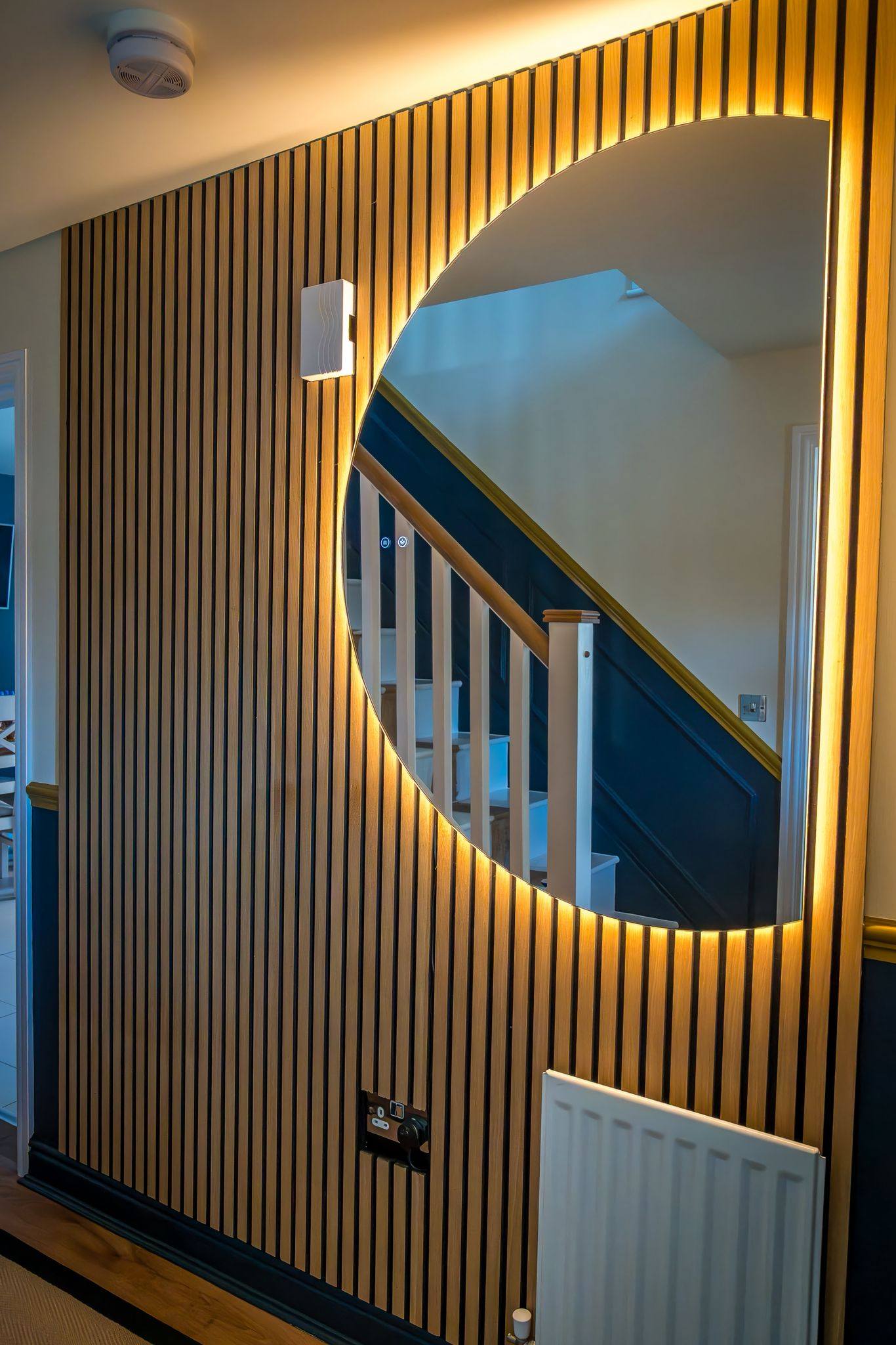 Curved oak slat wall with circular mirror cutout, navy panelling, gold trim