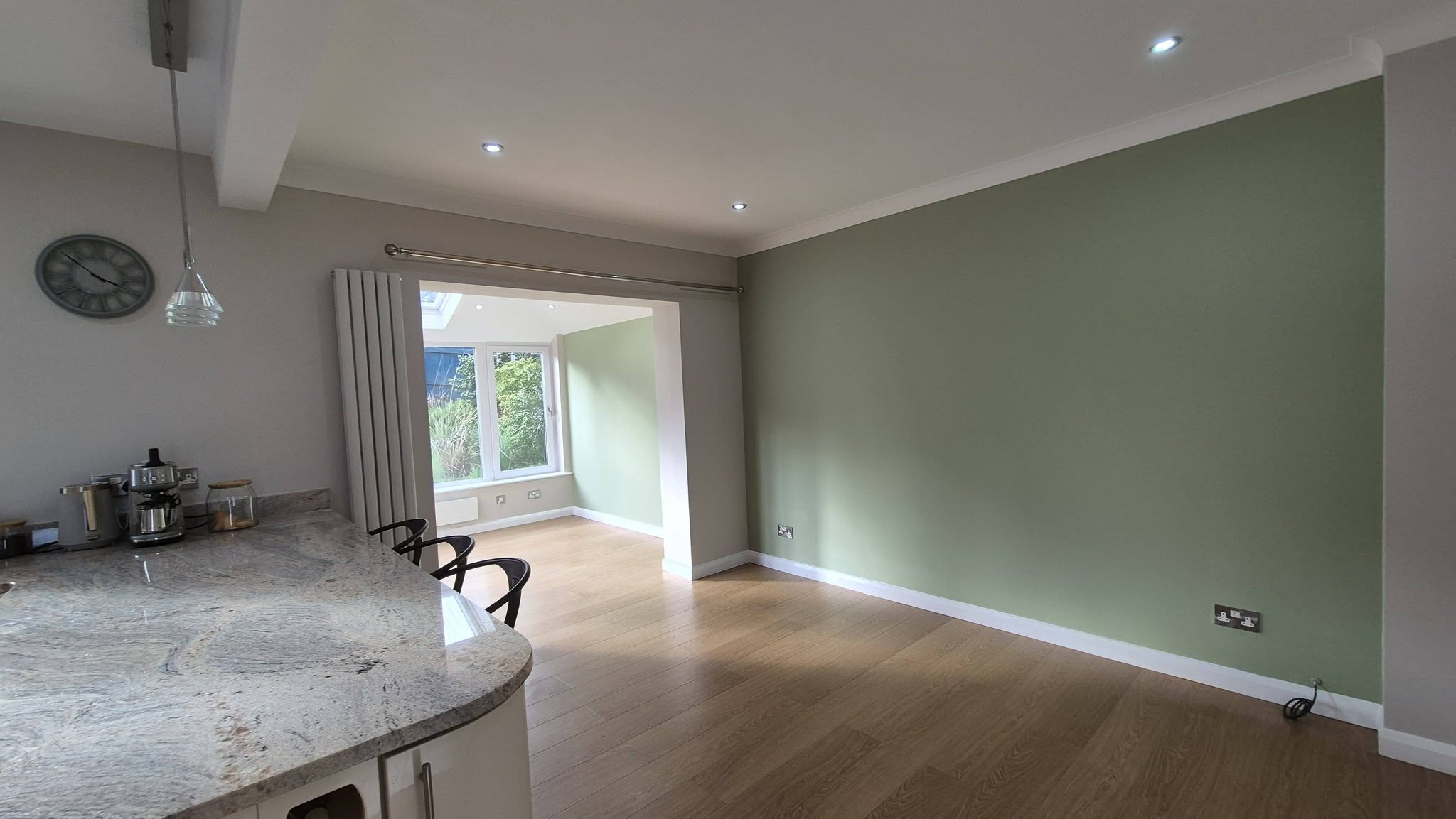 Open-plan kitchen with sage green feature wall and oak flooring